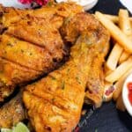 Crispy chicken drumsticks and fries on a black platter with ketchup.