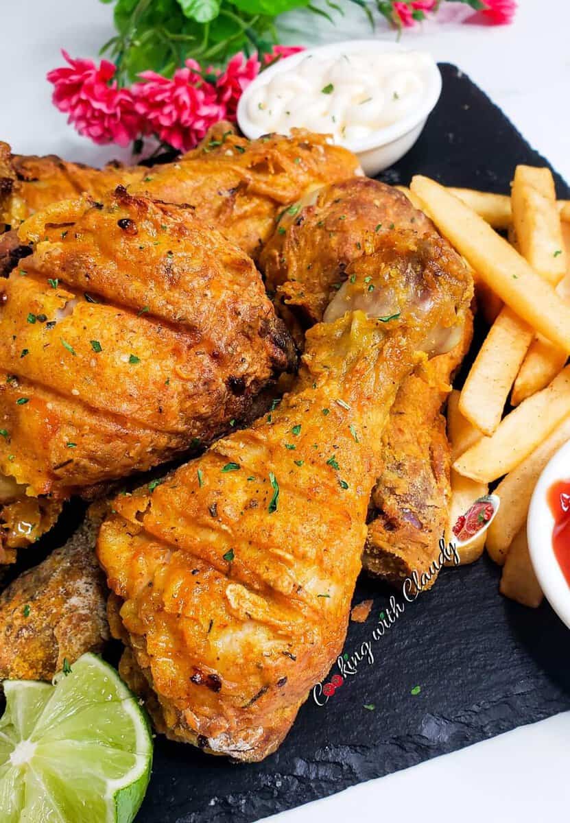 Crispy chicken drumsticks and fries on a black platter with ketchup.