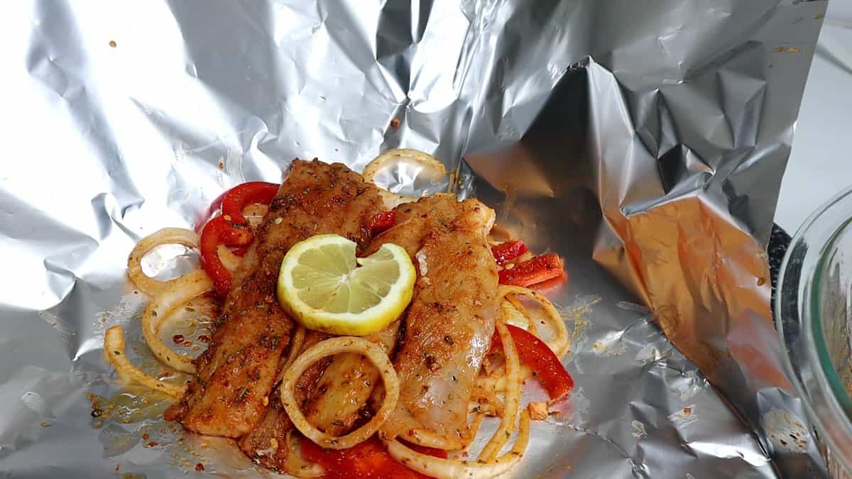 Aluminum foil sheet topped with fish over vegetables.