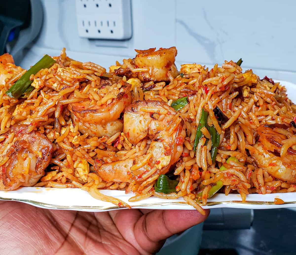 Person holding a plate piled with Shrimp Fried Rice.