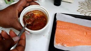 Spoon in a bowl of marinade next to salmon.