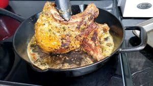 Tongs flipping pork chops in a pan.