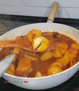 Wooden spoon lifting potatoes from a pan.