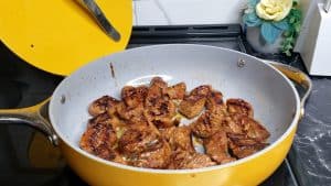 Beef cooking in oil in a yellow skillet.