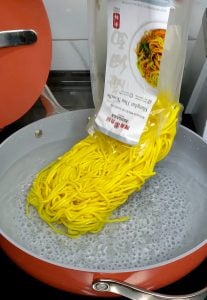 Package of Shanghai-style noodles pouring into a pan of water.