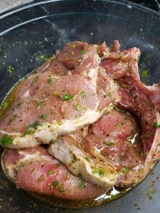 Pork chops marinating in a glass bowl.