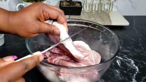 Person using a knife to score the fat on pork chops.