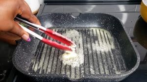 Tongs moving butter around a grill pan.