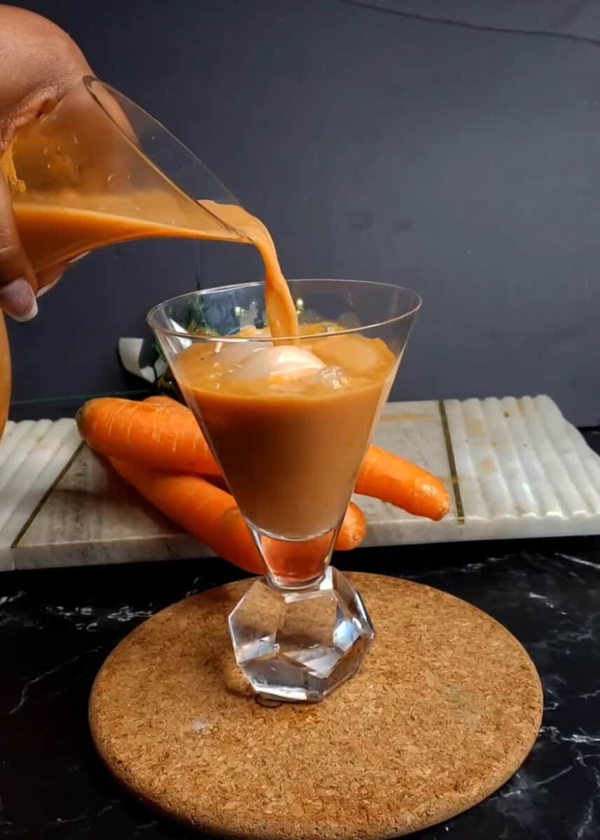 Pitcher pouring Jamaican Carrot Juice into a glass.