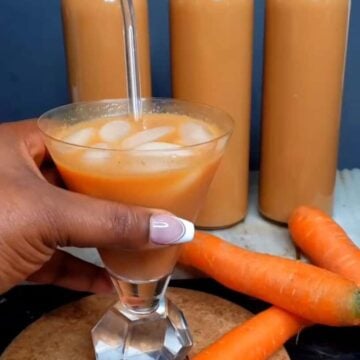 Hand holding a class of Jamaican Carrot Juice with ice.