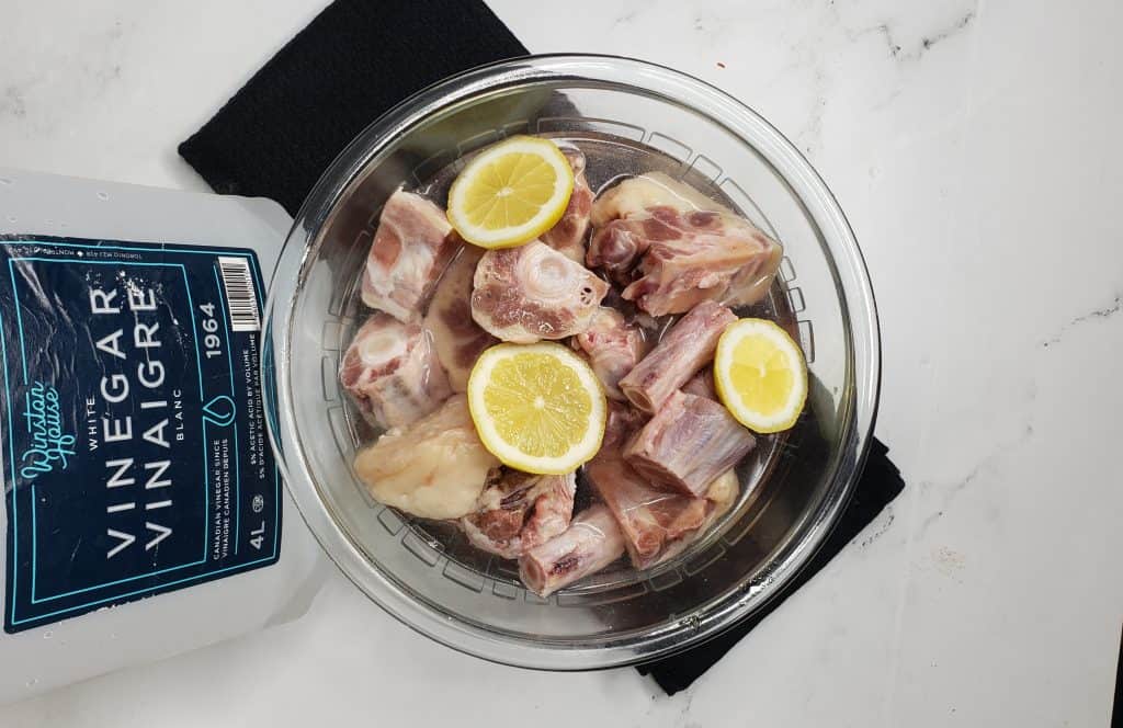 Glass bowl of oxtail, water, vinegar, and lemon.