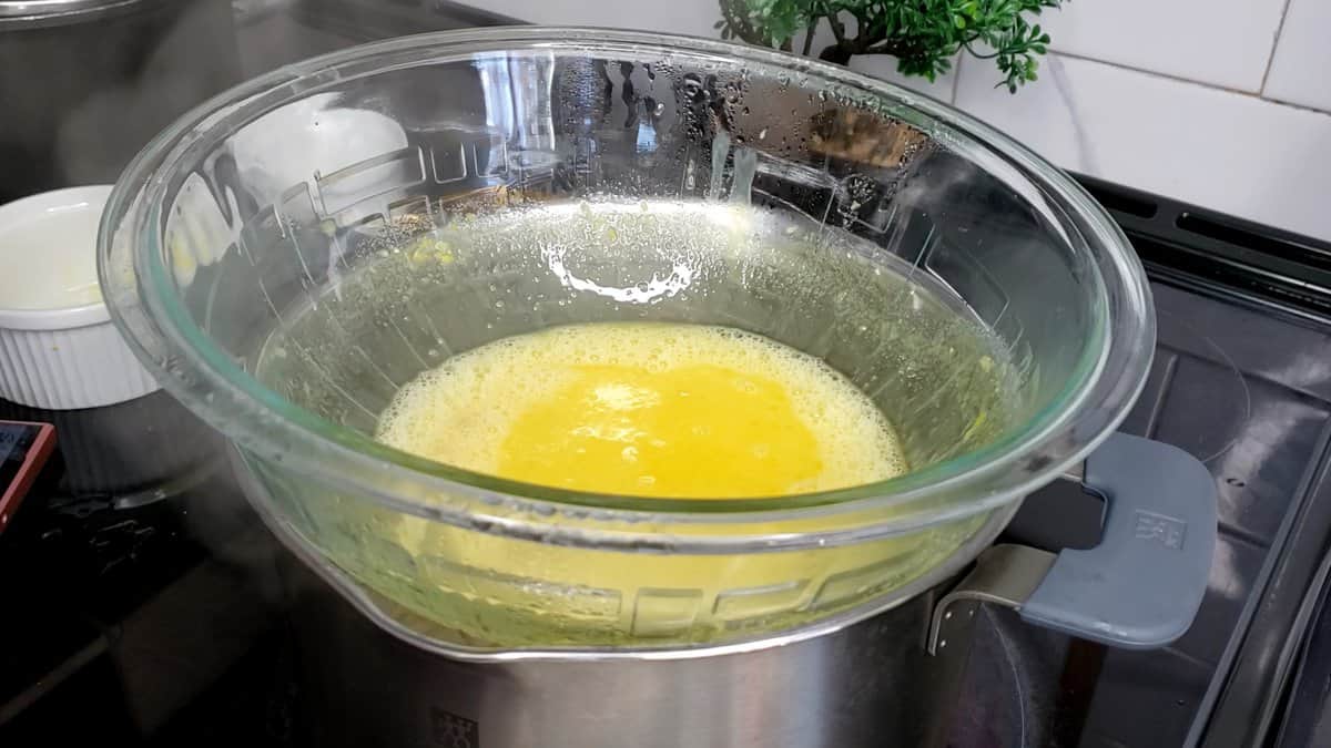 Yellow ingredients in a glass bowl set on a pot.