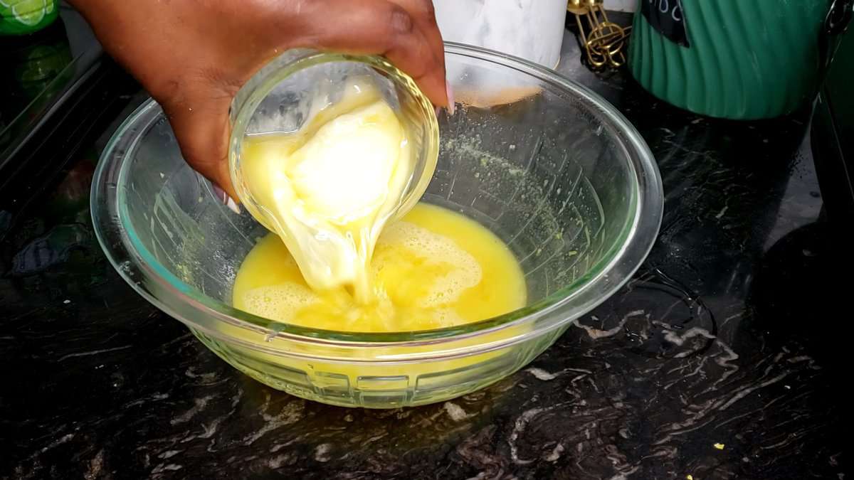 Person pouring softened butter into a glass bowl.