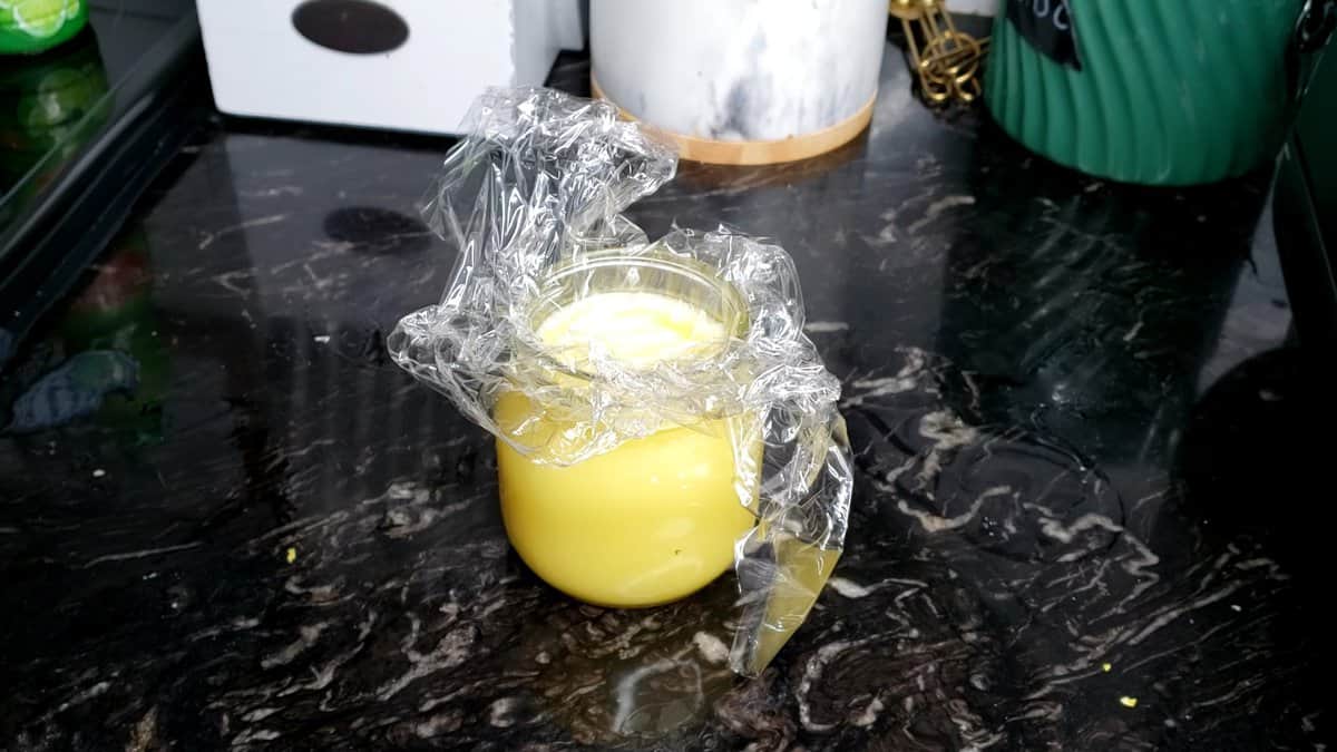 Glass jar of lemon curd topped with plastic.