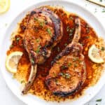 Two Baked Pork Loin Chops on a white plate with lemon slices.