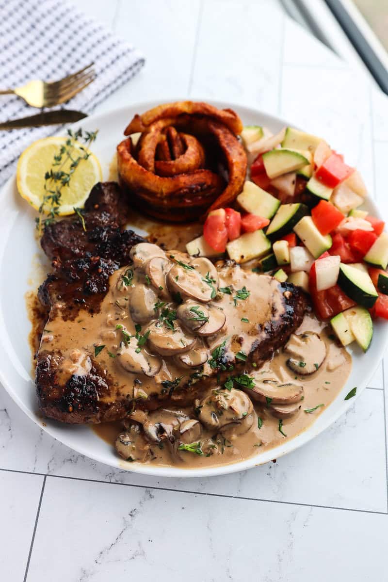 Plate with vegetables next to a steak coated in a Creamy Mushroom Sauce.