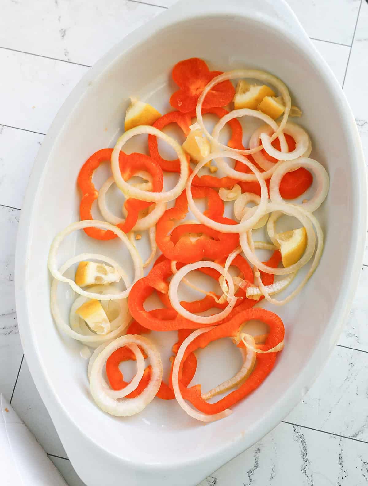 Pan lined with slices of onion, bell pepper, and lemon.