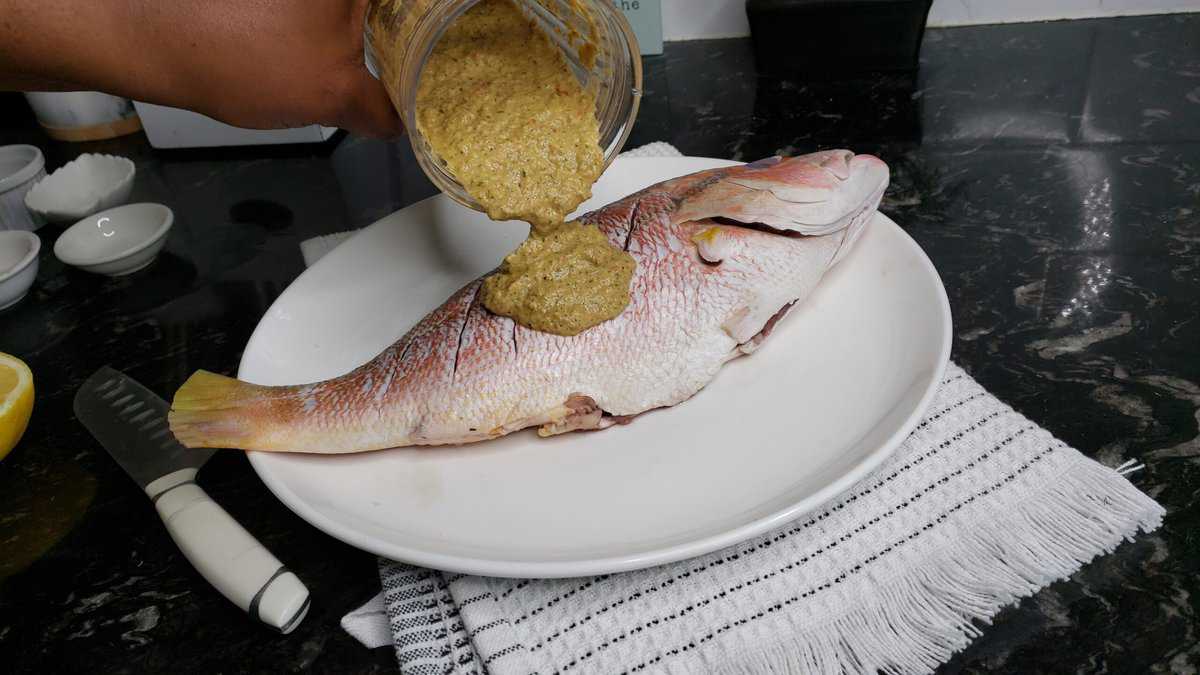 Person pouring marinade onto a red snapper.