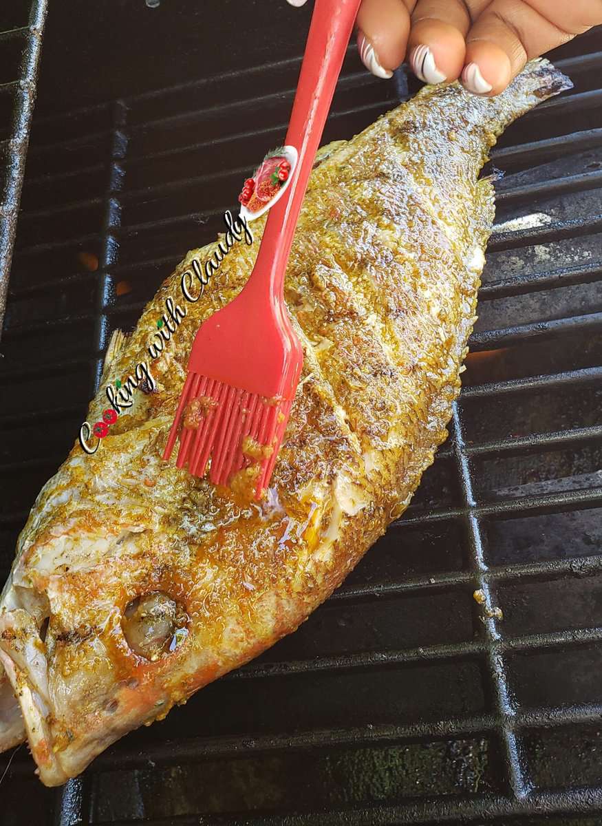 Brush basting sauce onto a red snapper on a grill.