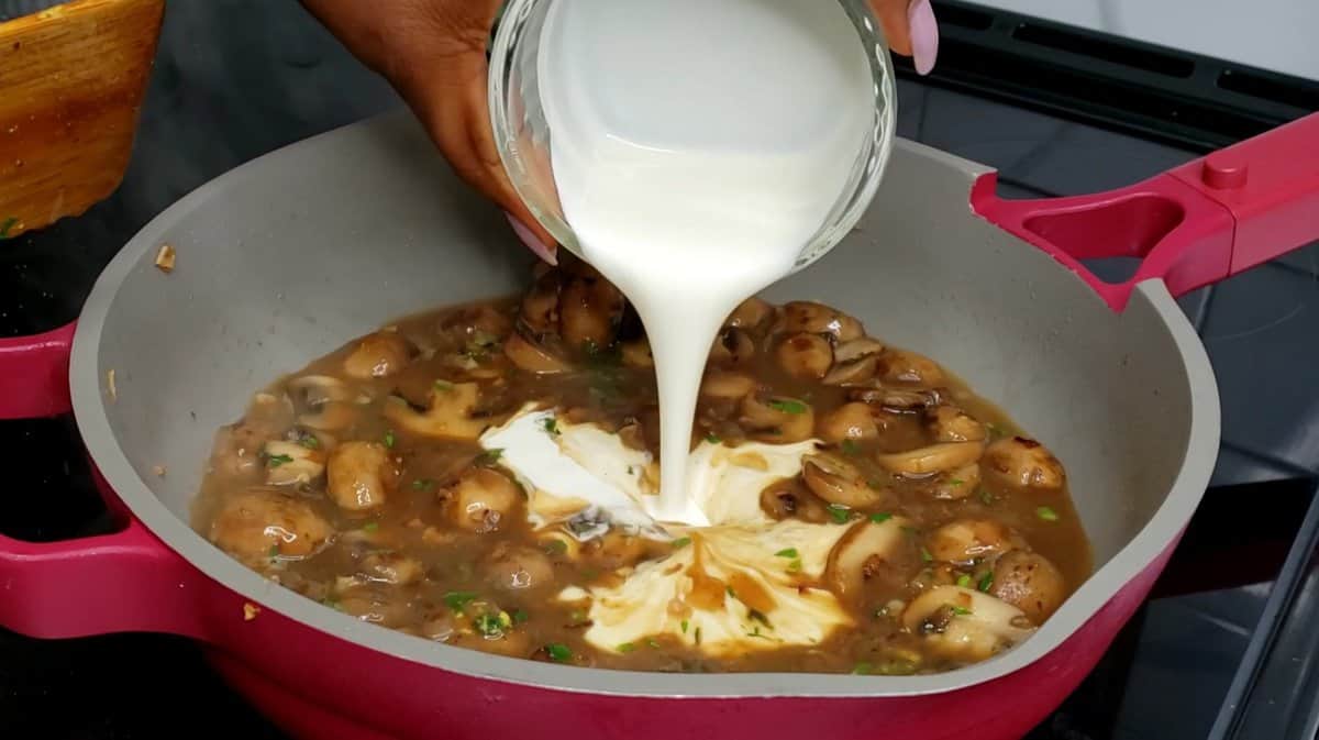 Person pouring heavy cream into a pot with a mushroom sauce.