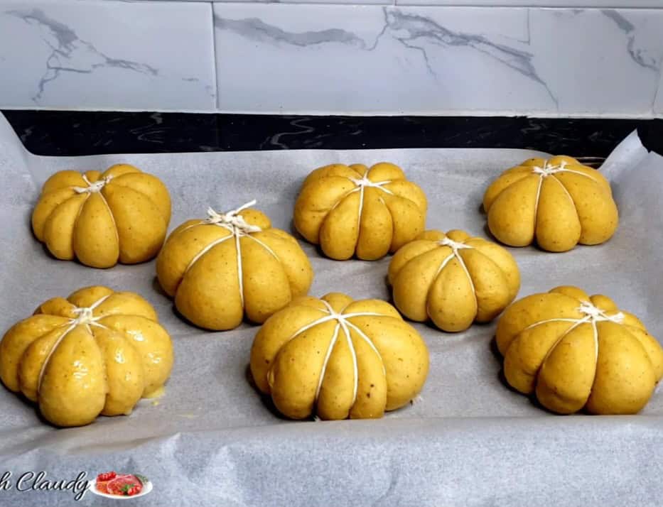 Dinner roll dough tied with twine on a parchment-lined baking dish.