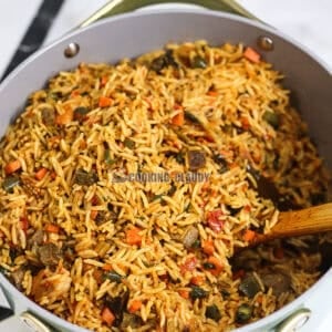 Wooden spoon stirring a pan of Cameroonian Jollof Rice.