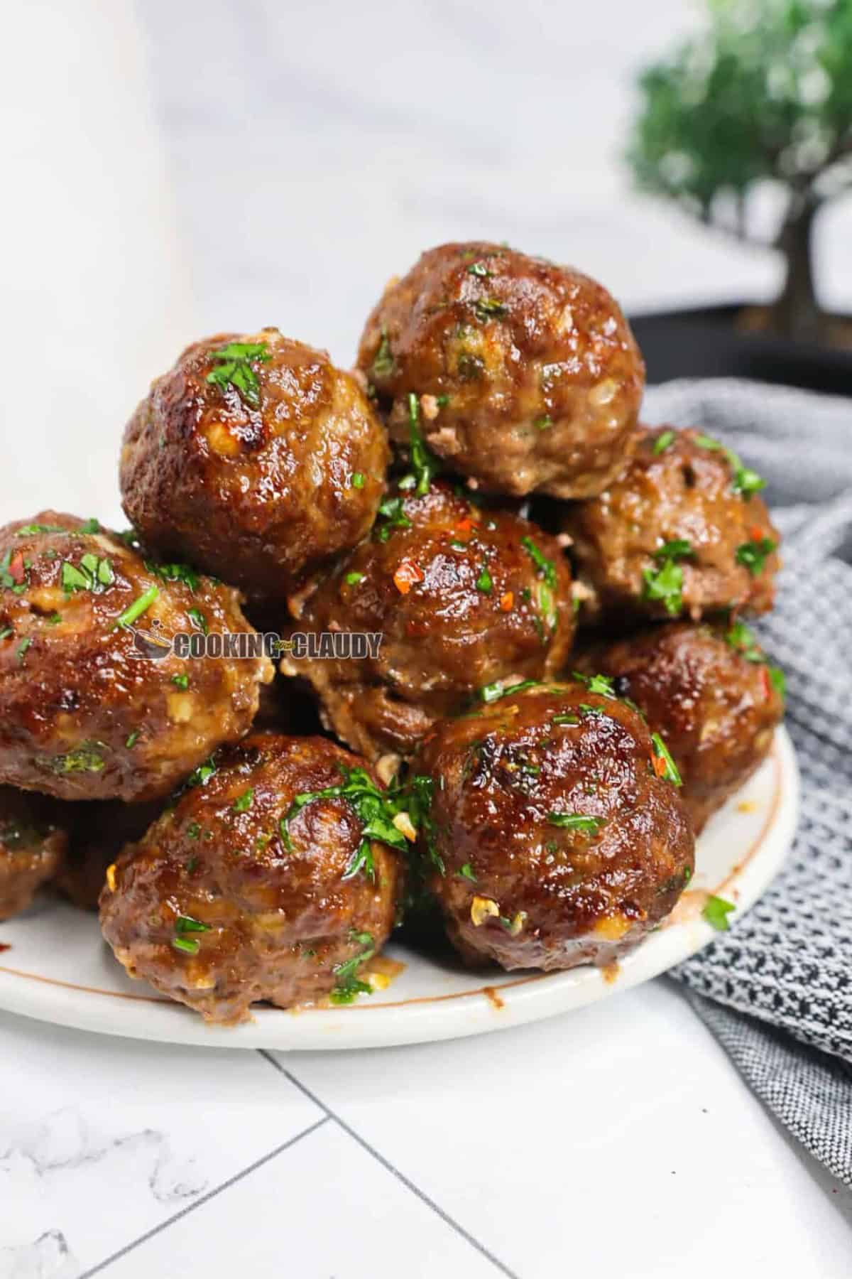 juicy baked meatballs stacked on each other, served on a plate. 