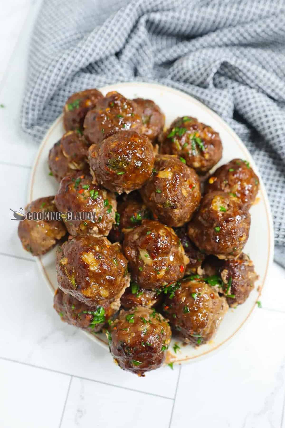 juicy baked meatballs stacked on each other, served on a plate. 