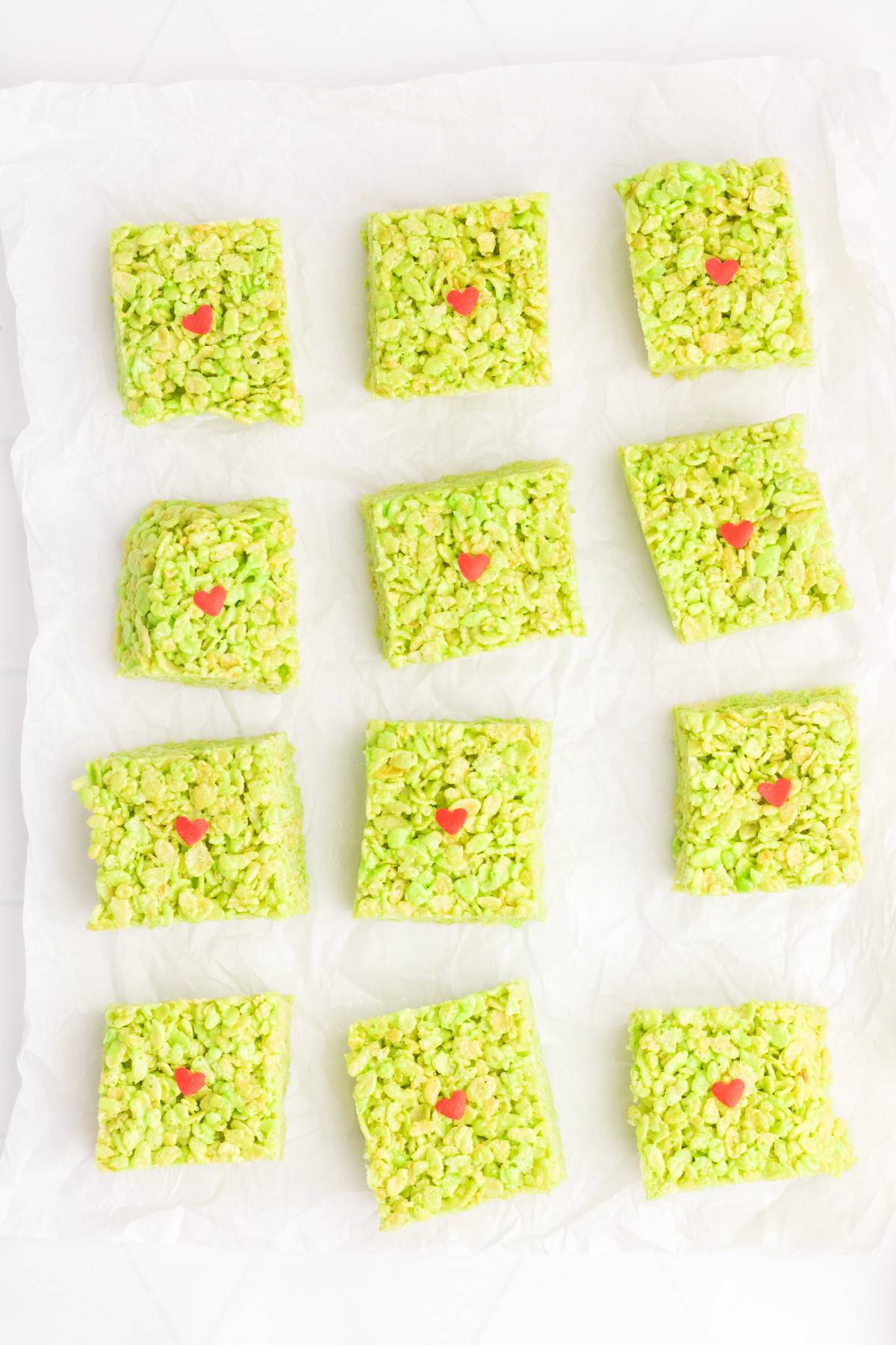 Grinch Rice Krispie treats cut into squares, with a heart sprinkle in the middle. 