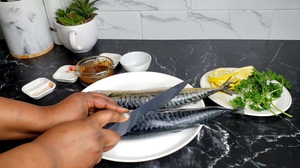 Person cutting slits into the side of mackerel.