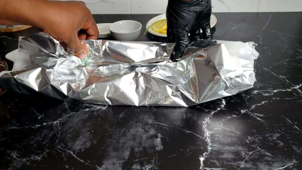 Person rolling aluminum foil over mackerel.