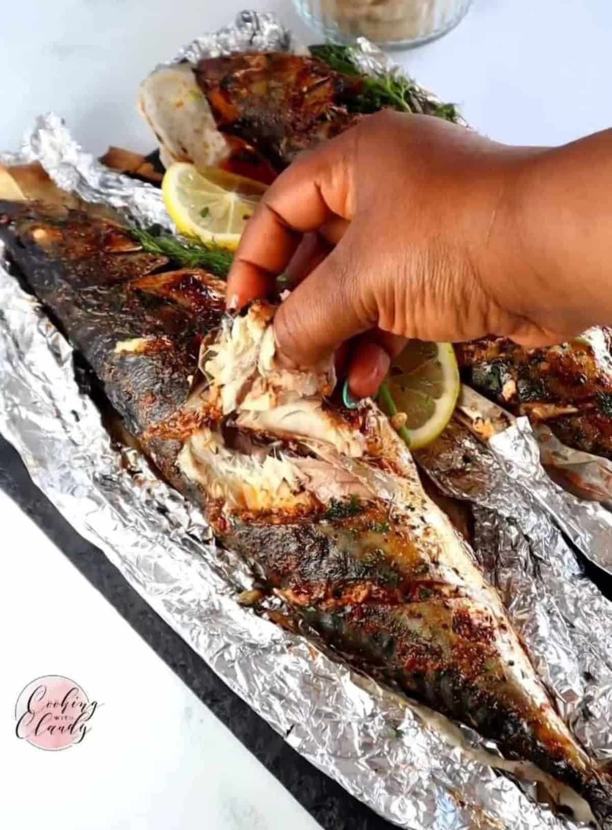 Person pulling some meat off of an Oven-Baked Whole Mackerel.