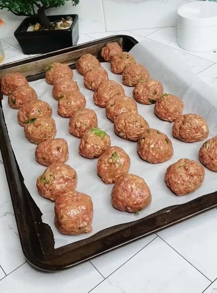 lined up uncooked meatballs on a baking sheet