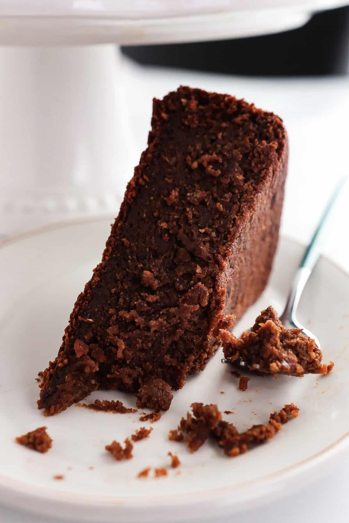 A slice of Jamaican rum soaked fruit cake with a spoon on a white plate. 