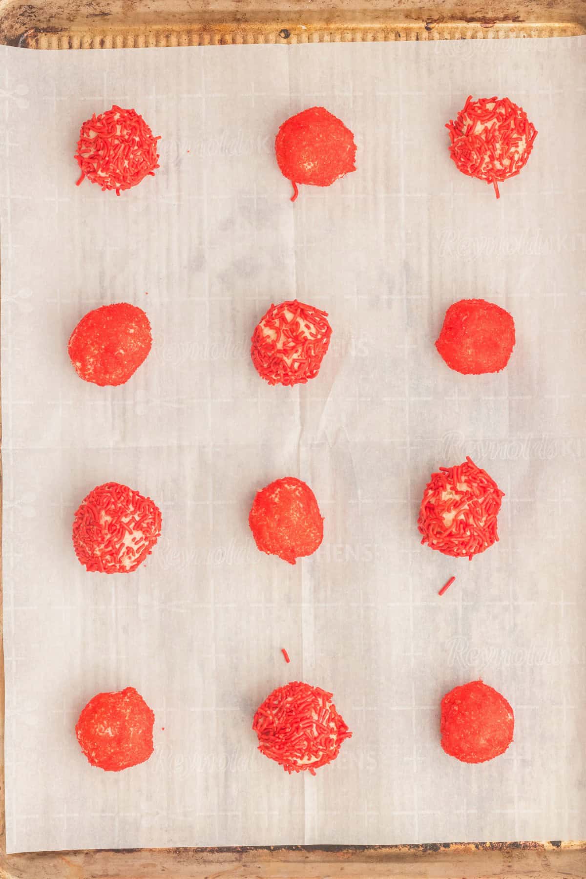 Cookie dough balls covered in red colored sprinkles. 