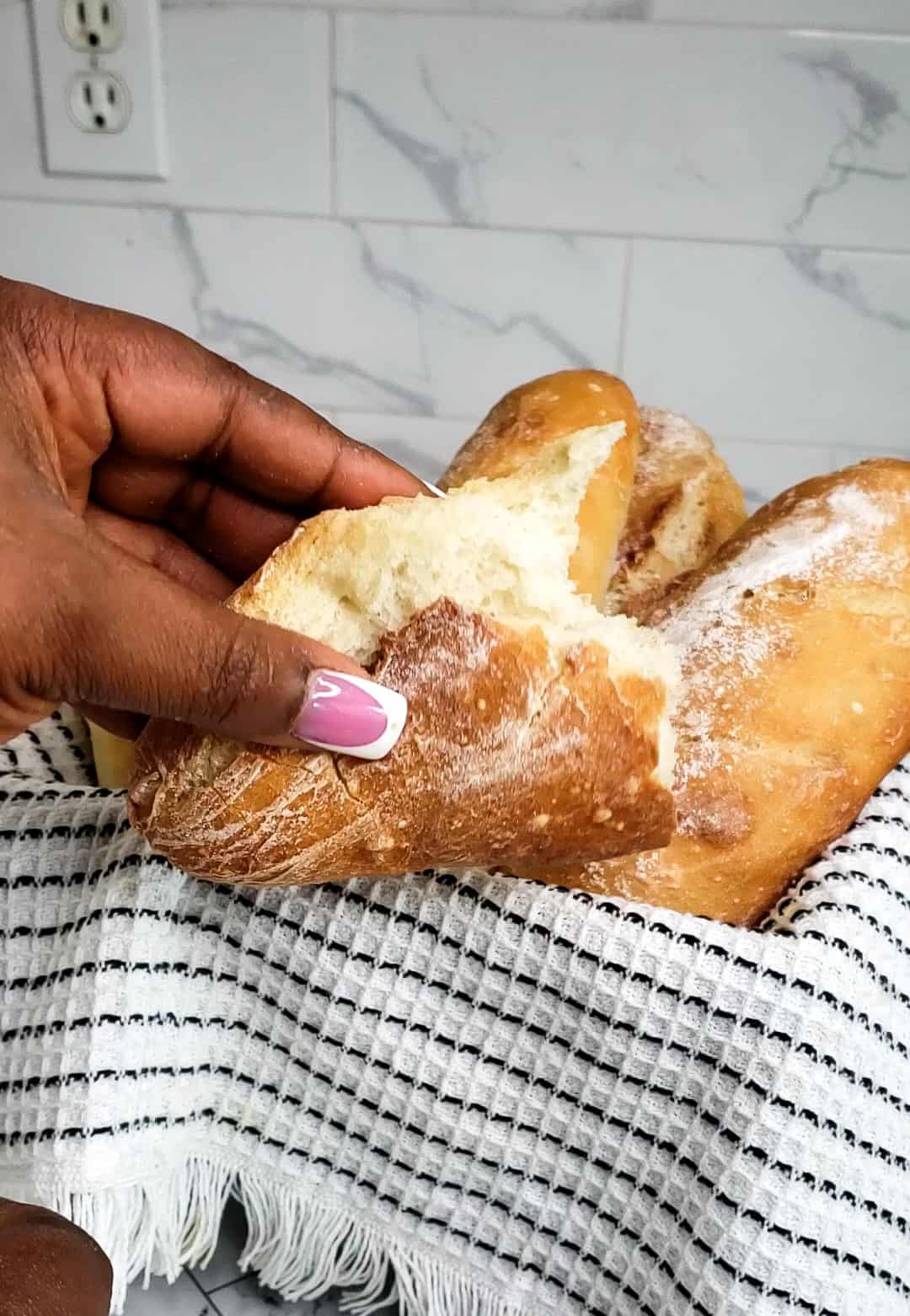 holding a piece of no knead baguette torn from a basket of baguettes. 