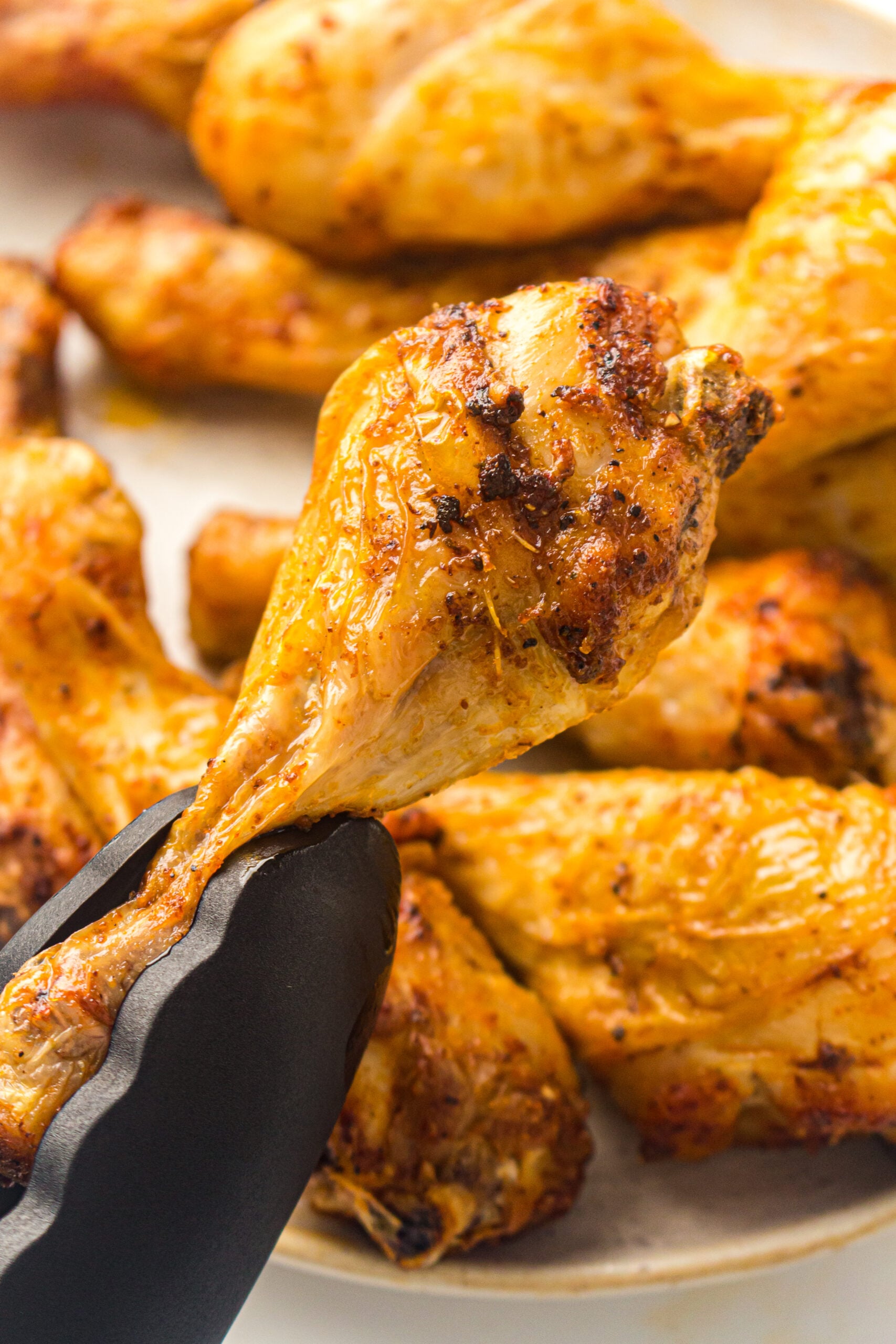 air fryer chicken drumsticks on a plate with a tong carrying a drumstick.