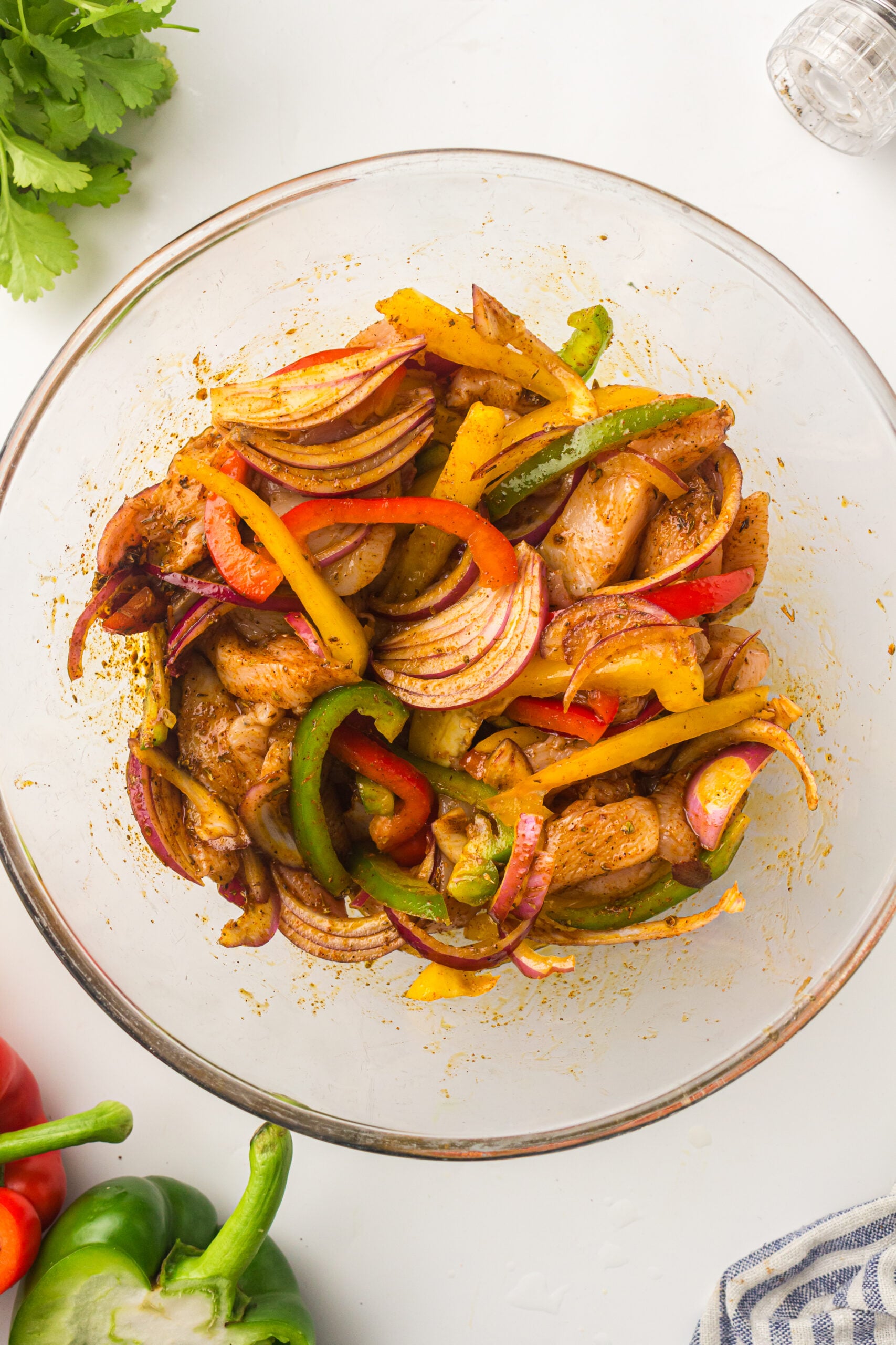Chicken and sliced peppers tossed with fajita seasoning in a glass mixing bowl