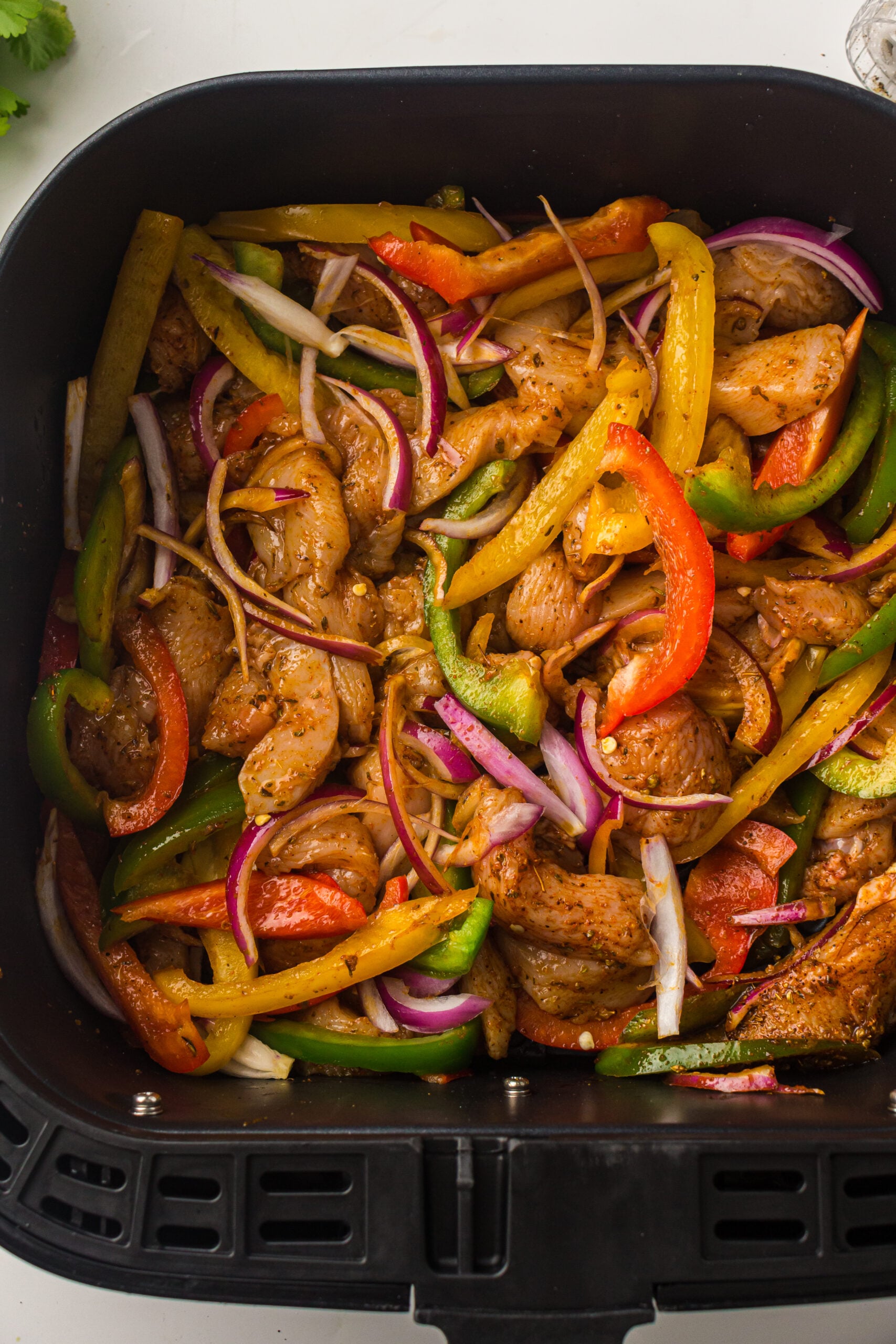 Seasoned chicken and peppers spread in a single layer in the air fryer basket