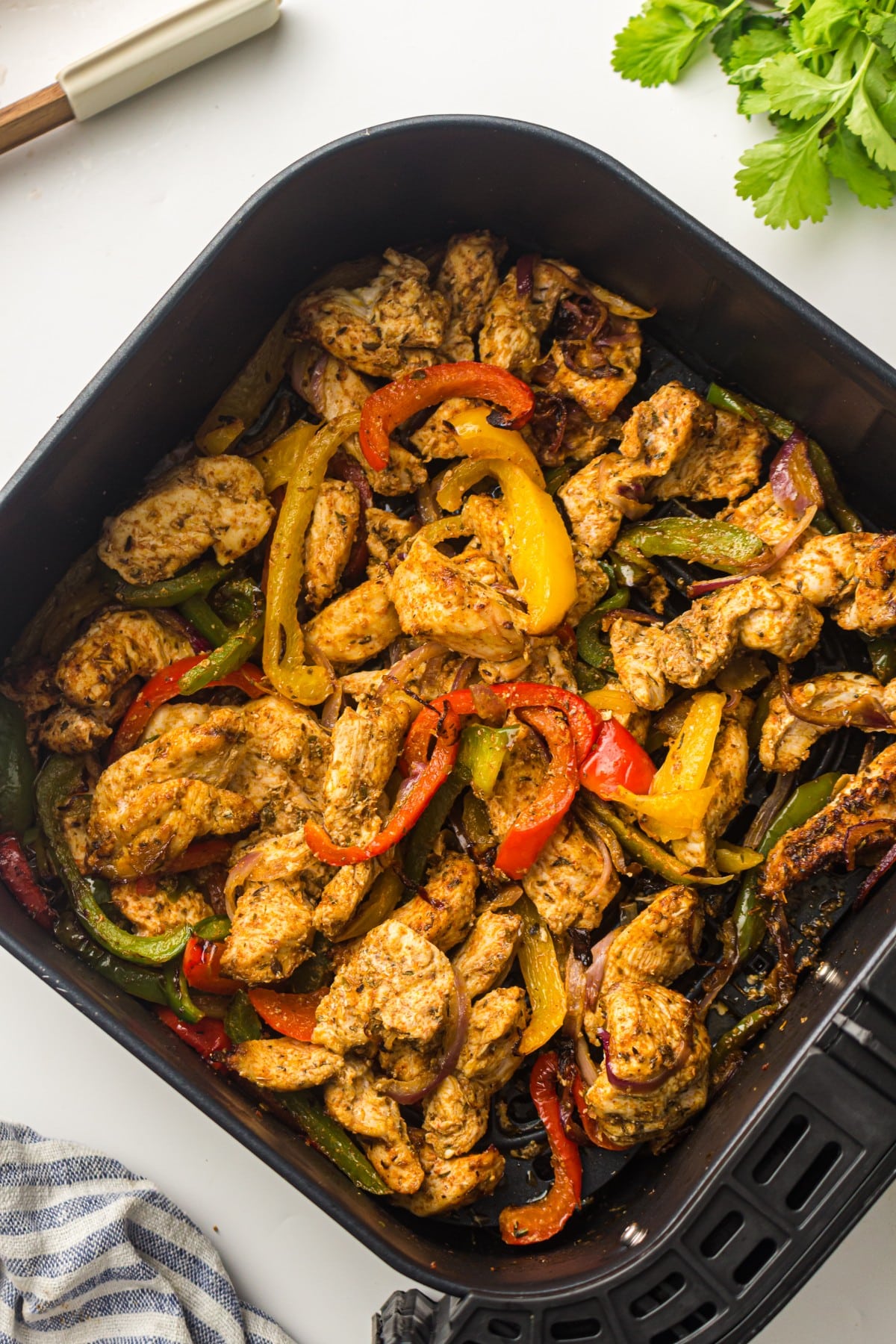 Close-up of seasoned chicken strips with red, yellow, and green peppers in and air fryer for fajitas
